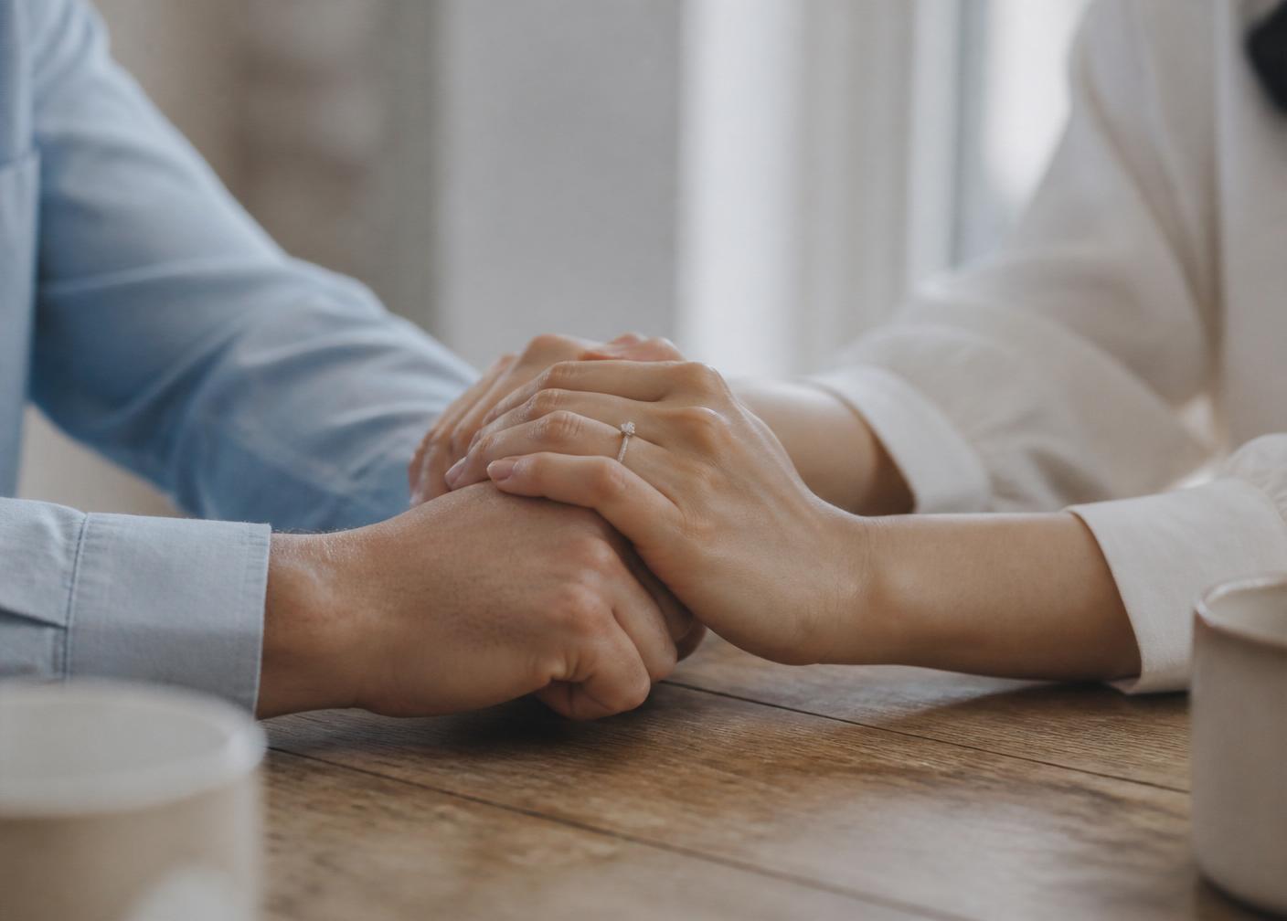 Mãos de um casal entrelaçadas sobre uma mesa de madeira, gesto de reconciliação